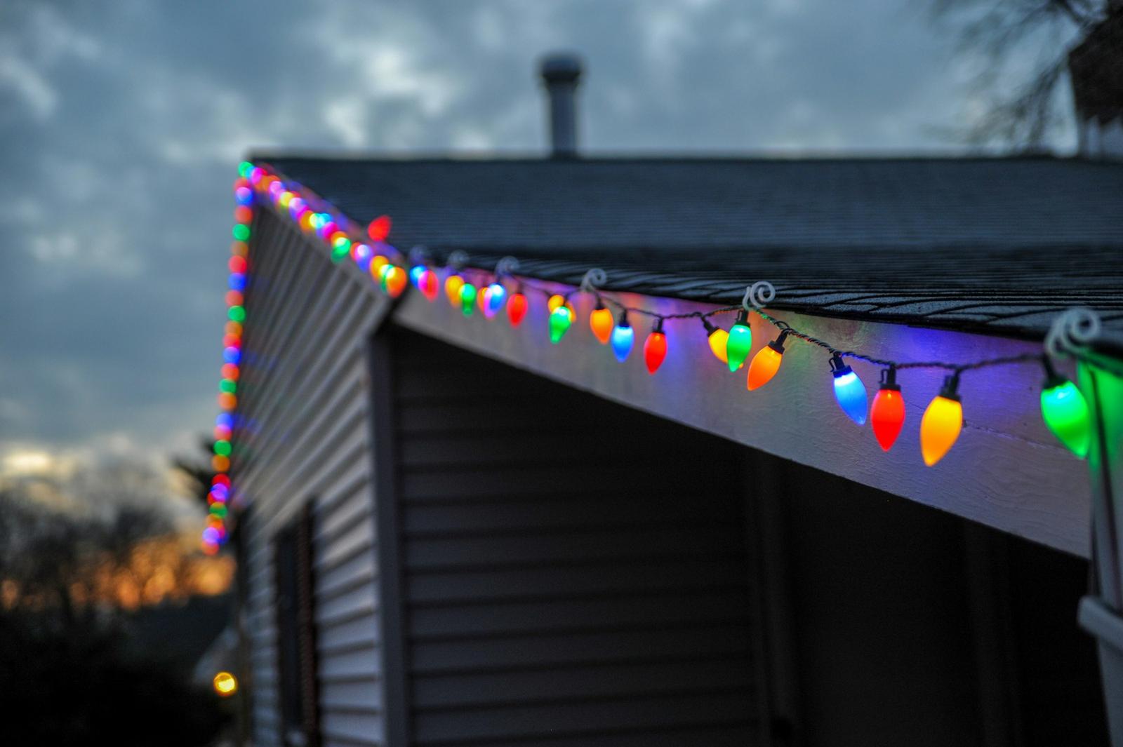 Close-up of colorful Christmas bulbs along a roof edge at dusk